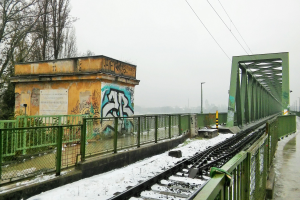 Ein schneebedeckter Bahngleis mit Graffiti an der Seite, umgeben von Gelöndern, Pfosten, Lichtern, Dröhnen und Bäumen, unter einem sichtbaren Himmel.