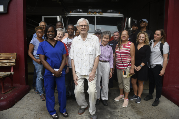 Eine Gruppe von Freiwilligen vor einem Feuerwehrauto, mit einer Bank auf der linken Seite und einer Wand im Hintergrund.