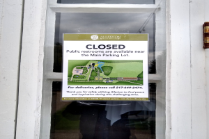 Glasstür mit einem Schild, auf dem "Geschlossene öffentliche Toiletten in der Nähe des Hauptparkplatzes" steht und ein unklares Objekt auf der rechten Seite.