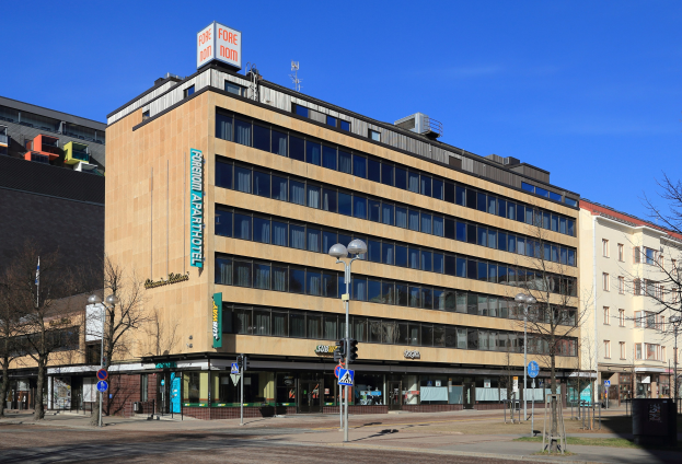 Großes Gebäude mit zahlreichen Fenstern, als Fore Inn Hotel Berlin identifiziert, umgeben von Straßeninfrastruktur einschließlich Pfosten, Lampen, Signalen, Schildern, Bäumen und einem bewölkten Himmel.