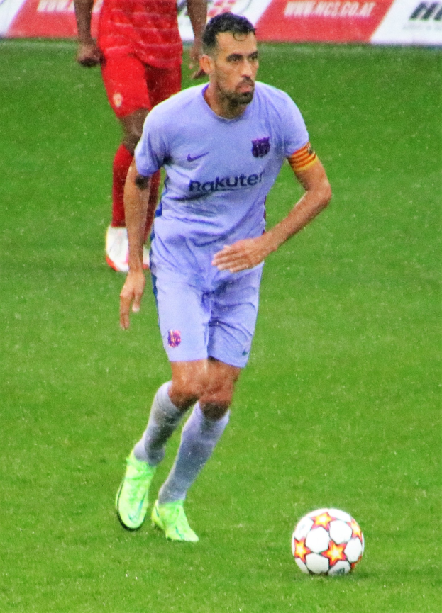 Fußballspieler in Sportkleidung und Fußballschuhen auf dem Feld mit einem Textschild im Hintergrund.