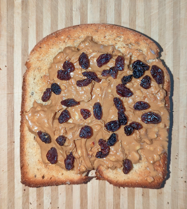 Ein Stück Brot mit Erdnussbutter und Rosinen auf einer hölzernen Oberfläche.