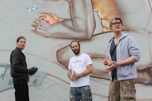 Menschen stehen mit Farbsprühflaschen vor einer graffiti-bedeckten Wand.