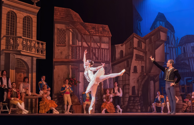 Zwei Tänzer performen auf einer Bühne im Royal Opera House in London, mit einem Publikum, das auf Stühlen sitzt und steht.