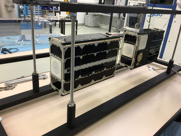 Ein Mann arbeitet an einem Satelliten in einem Labor, mit verschiedenen Gegenständen auf dem Tisch und NASA-brandeter Ausrüstung im Hintergrund.