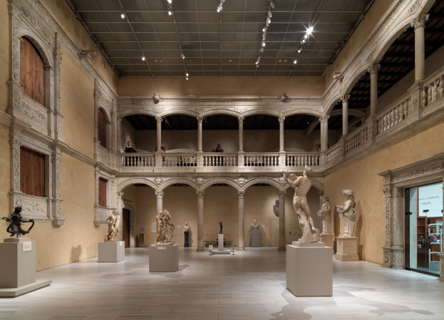 Großer Raum in einem Museum mit zahlreichen Statuen und Skulpturen auf Sockeln, architektonischen Elementen wie Wänden, Säulen und Geländern, Deckenbeleuchtung und einigen Besuchern.