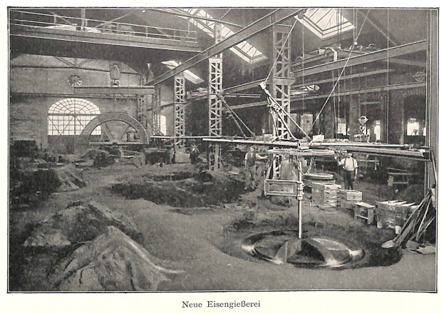 Schwarze und weiße Fotografie eines Fabrikinneren mit Arbeitern, die Maschinen bedienen, umgeben von Metallstangen und -stangen, beschriftet mit "Neue Eisenglebeerei, die erste Fabrik in Deutschland" unten.