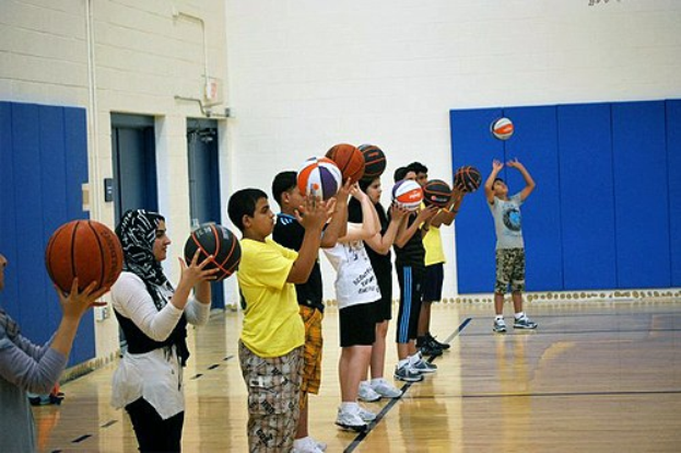 Jugendliche mit Basketballs auf einem Basketballfeld während eines Camps, mit Türen und einer Wand im Hintergrund.