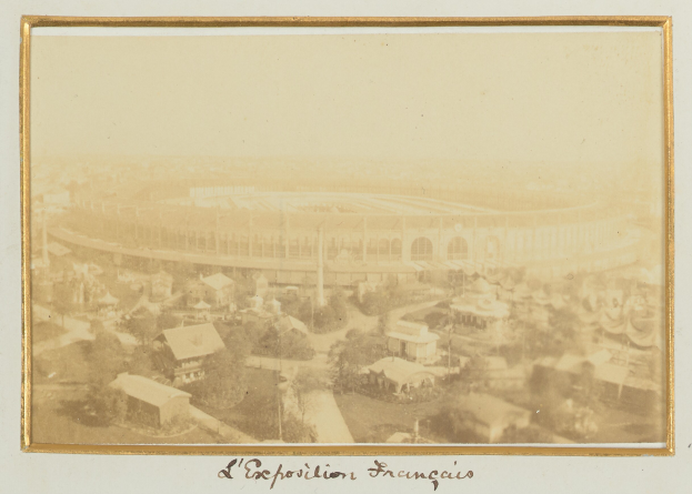 Altes Schwarz-Weiß-Foto eines Stadions, umgeben von Gebäuden, Bäumen und Masten, mit Text unten.