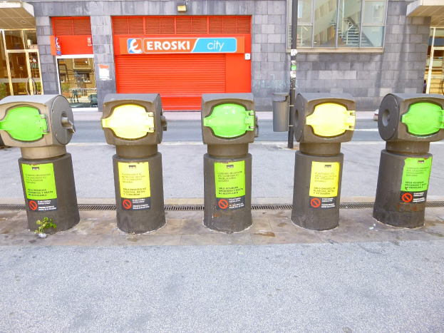 Reihe von Parkautomaten an einer Straße mit einem Gebäude mit Glasfenstern und einem Rollladen mit Text daneben.