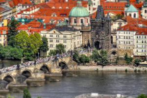 Eine Stadtansicht mit zahlreichen Gebäuden, einem markanten Turm, Bäumen, Menschen, einem Fluss und einer Brücke, die den Fluss überquert.