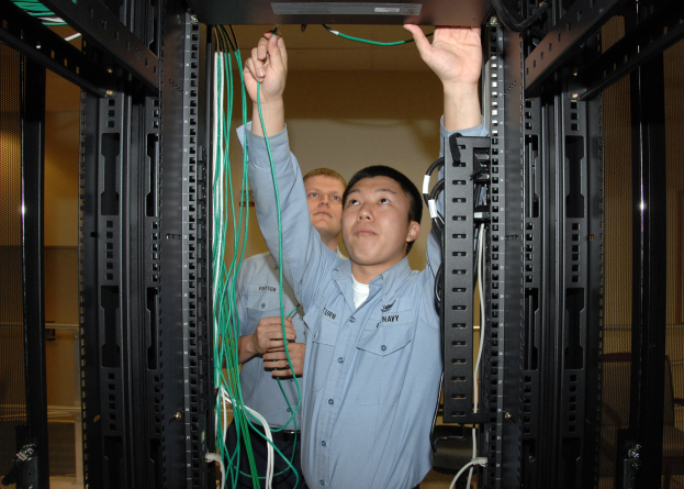 Zwei M├Ąnner arbeiten an einem Server in einem Rechenzentrum mit Kabelregalen und einer Wand im Hintergrund.