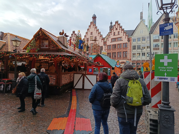 Menschen, die auf einem Kopfsteinpflasterweg neben einem Weihnachtsmarkt in Nürnberg, Deutschland, gehen, mit Laternenmasten, Texttafeln und Gebäuden im Hintergrund bei einem bewölkten Himmel.