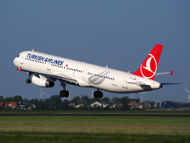 Turkish Airlines Airbus A330-300 steigt von Frankfurt Airport auf, mit Gras darunter, Gebäuden und Bäumen im Hintergrund, Windmühlen in der Ferne und einem klaren blauen Himmel.