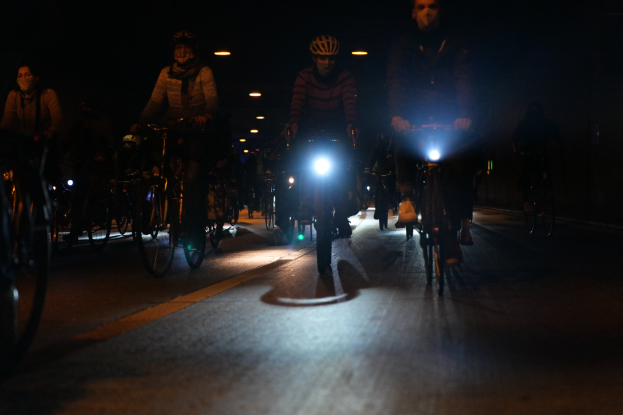 Eine Gruppe von Menschen, die nachts mit Fahrrädern eine Stadtstraße entlangfährt und Helme trägt.