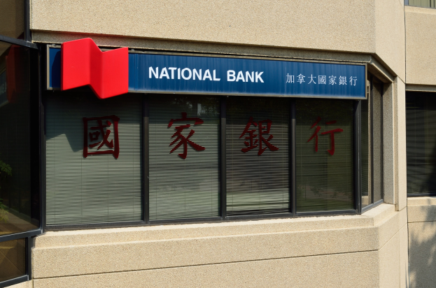 Ein modernes Gebäude mit Glasfenstern, die ein 'National Bank'-Schild in Englisch und Chinesisch sowie eine Pflanze links davon zeigen, was die Eröffnung einer neuen Filiale in Hong Kong ankündigt.