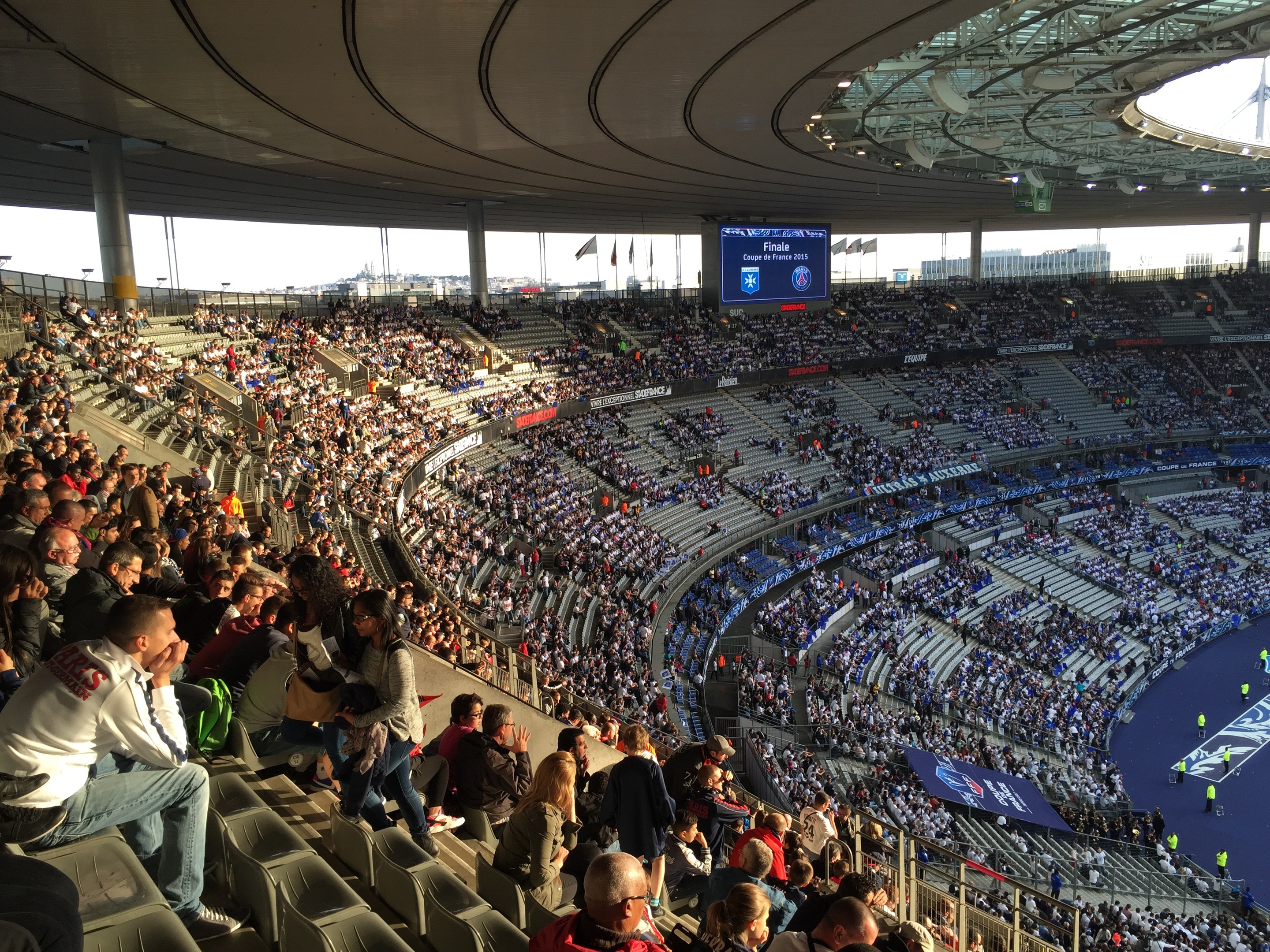 Große Menschenmenge in einem Stadion bei einem Förderball, mit einer Bühne auf der rechten Seite, Fahnen, Masten, einem Bildschirm und der Allianz Arena in München, Deutschland im Hintergrund.
