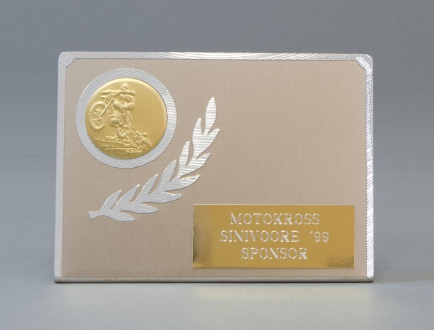 Eine goldene und silberne Visitenkarte mit Lorbeerkranz-Design, mittig im Bild mit Text, der wahrscheinlich den Namen des Sponsors angibt.