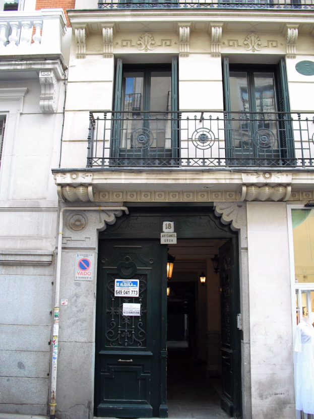 Ein Gebäude mit einer grünen Tür, Fenstern, Geländern, Lampen, Texttafeln, einem Rohr und anderen Gegenständen, mit einer Straße unten.