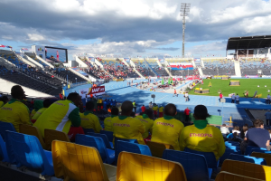 Ein volles Stadion mit Zuschauern bei einem Fußballspiel, mit Bannern, Anzeigetafel, Metallpfosten-Dach und einem bewölkten Himmel.